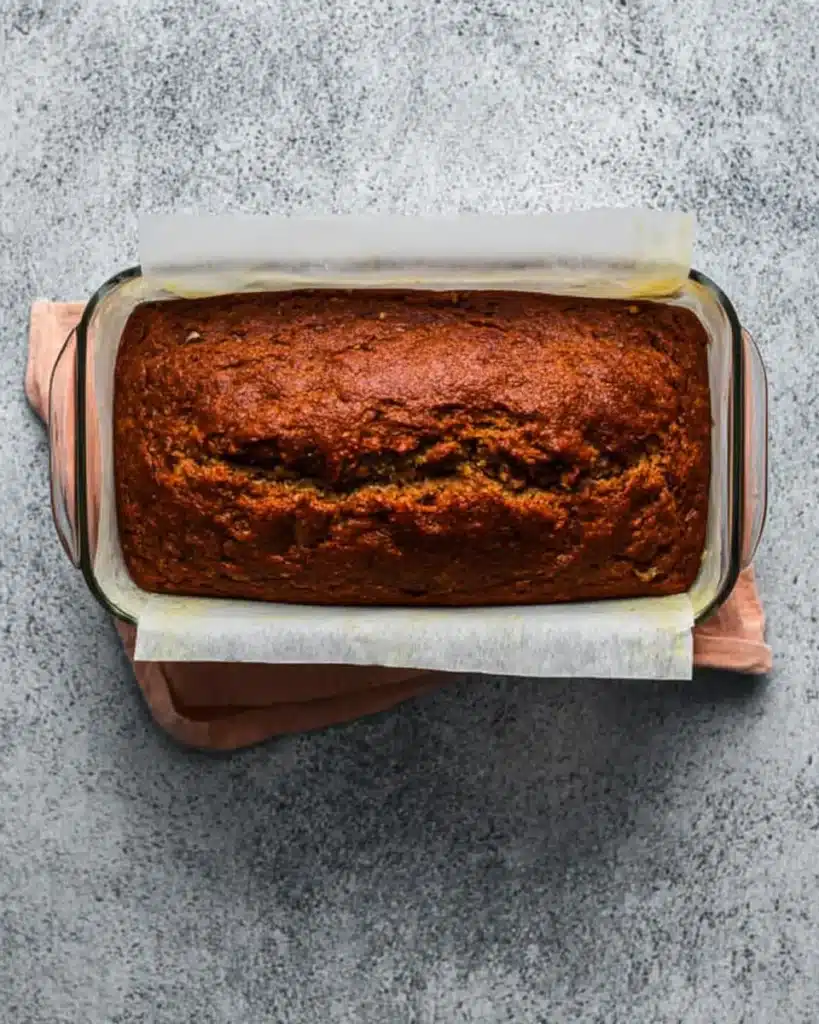 Date Nut Bread Recipe – Easy, Moist, and Nostalgic 9 Fully baked date nut bread loaf in a parchment-lined glass pan, resting on a rustic stone surface