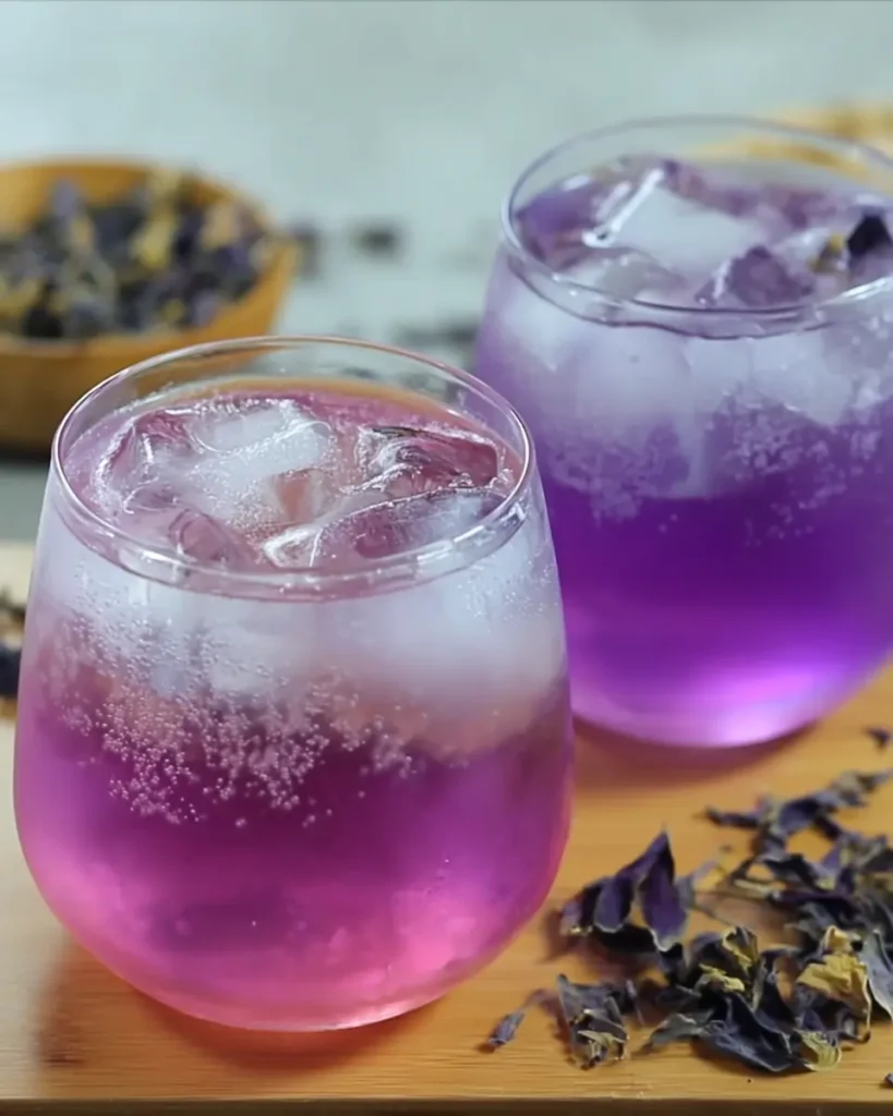 Butterfly Pea Tea Lemonade – Brilliant & Refreshing Recipe 13 Butterfly pea tea lemonade in two iced glasses with a vibrant purple-pink gradient, served with fizz and dried flowers on a textured table