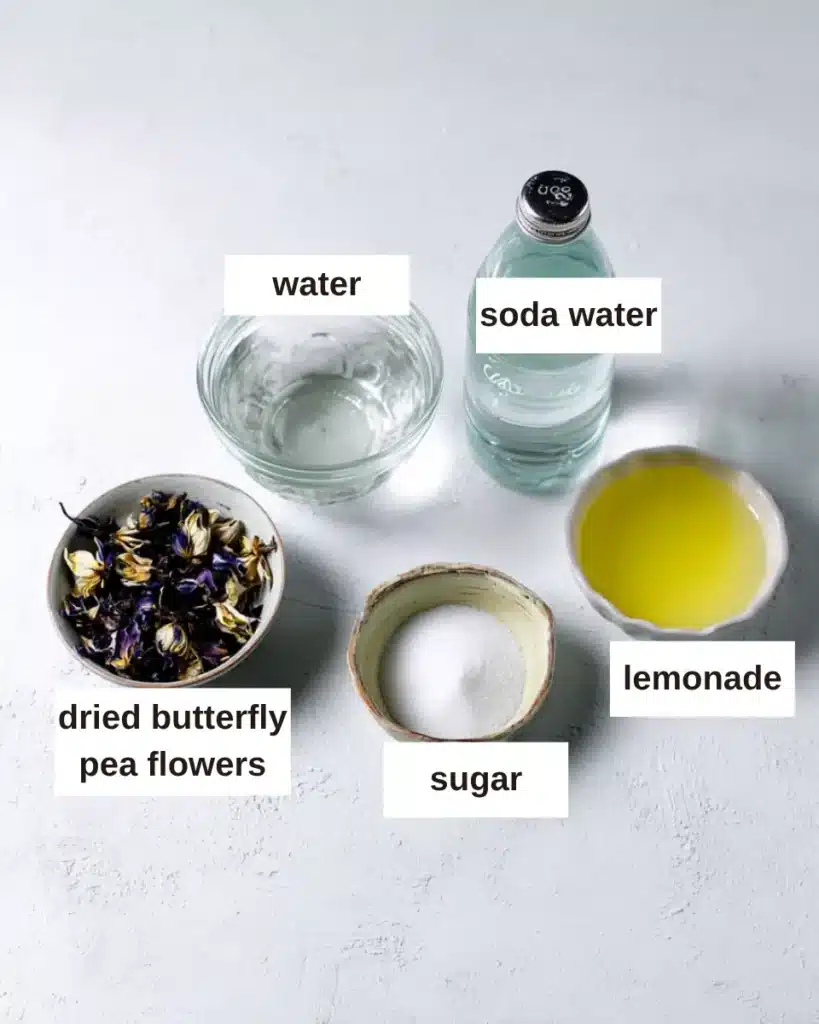 Butterfly Pea Tea Lemonade – Brilliant & Refreshing Recipe 14 Butterfly pea tea lemonade ingredients including dried butterfly pea flowers, lemon juice, sugar, soda water, and water on a clean white background