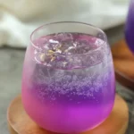 Butterfly Pea Tea Lemonade – Brilliant & Refreshing Recipe 18 Chilled butterfly pea tea lemonade with ice and bubbles in a clear glass on a natural surface