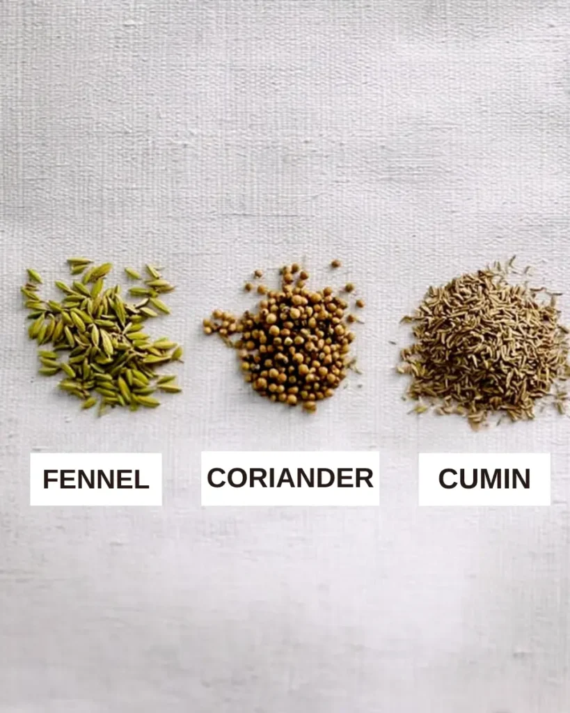 CFC tea recipe ingredients – coriander, fennel, and cumin seeds labeled and arranged on a light linen-textured surface