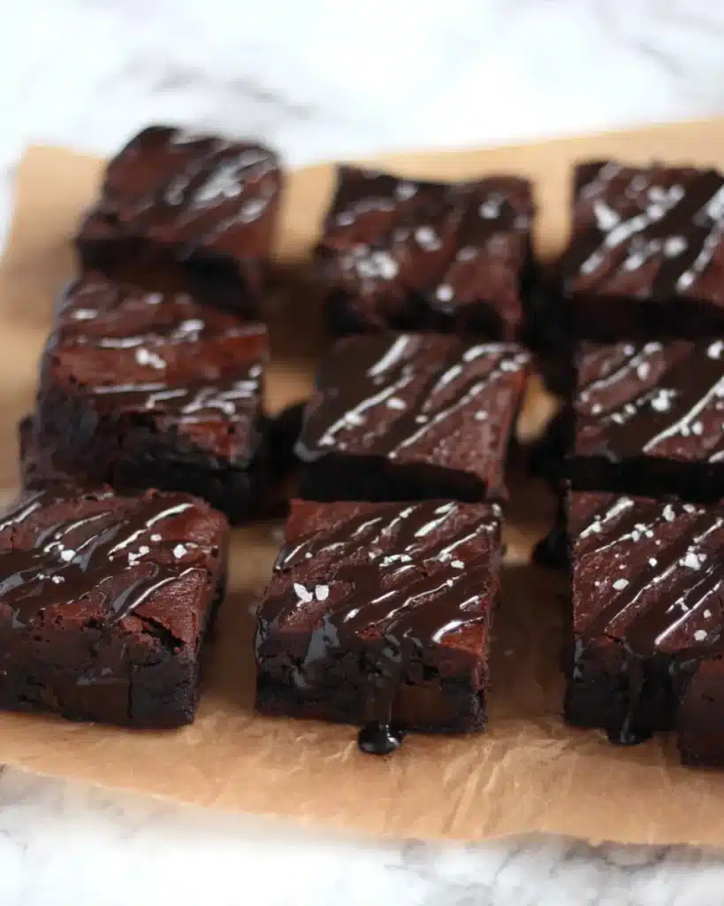 Overhead shot of sliced date brownies topped with chocolate glaze and sea salt, arranged in rows on parchment.