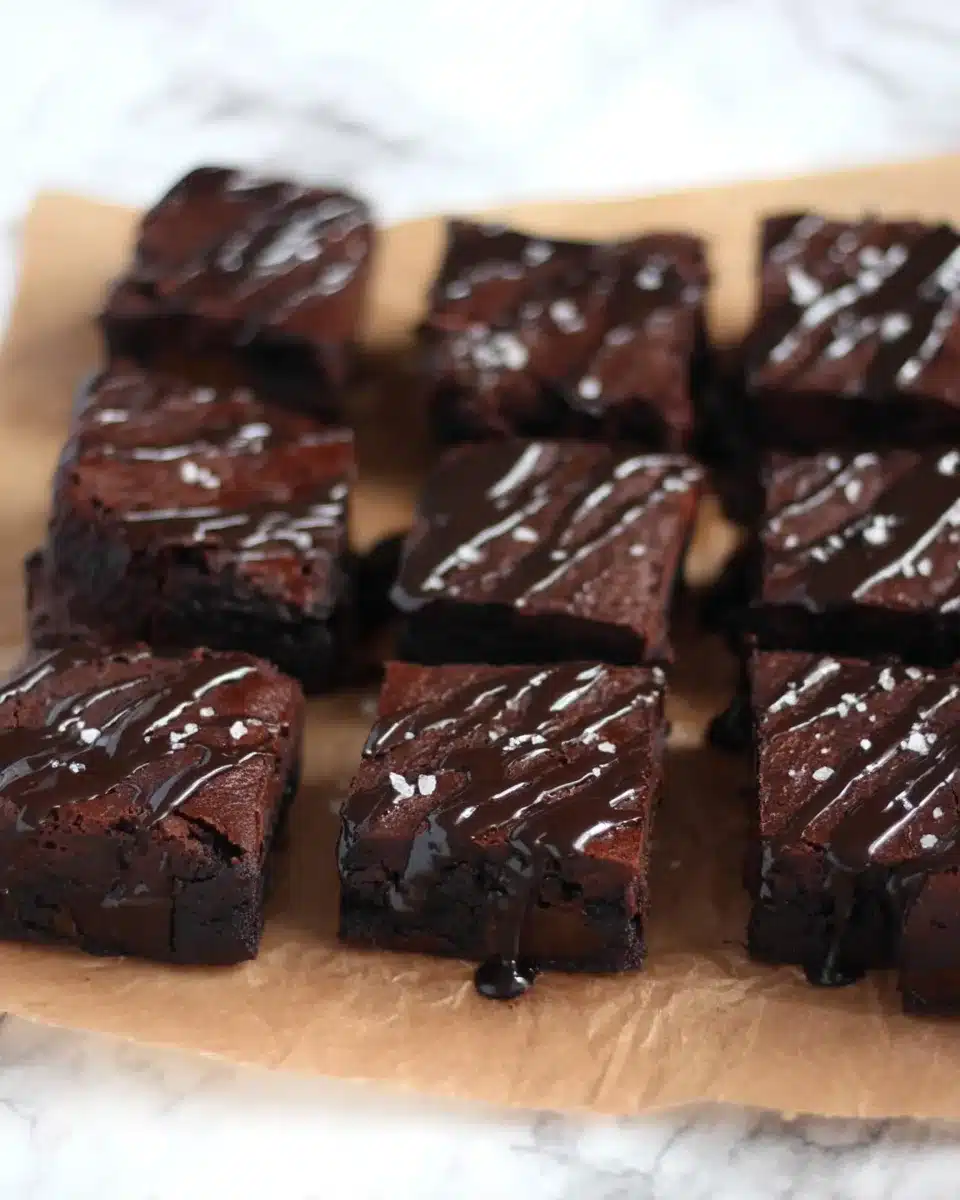 Overhead shot of sliced date brownies topped with chocolate glaze and sea salt, arranged in rows on parchment.
