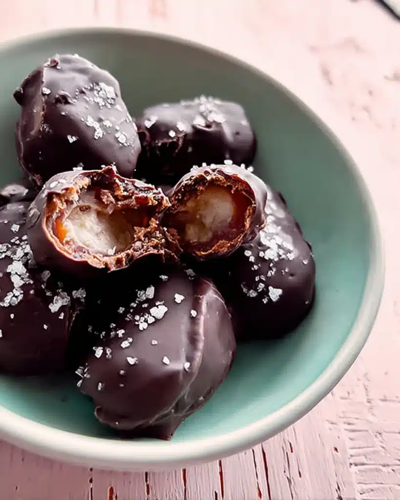 How to Make the Best Tahini Chocolate Date Dessert (Easy, Healthy & Irresistible) 5 Close-up of a chocolate-covered date with tahini filling and sea salt in a ceramic bowl