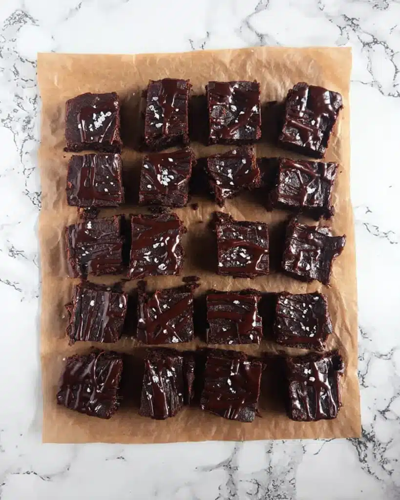 Date Brownies Recipe – Fudgy, Healthy, and Naturally Sweetened 6 Overhead view of chocolate date brownies drizzled with glaze and sea salt, arranged in rows on parchment paper.