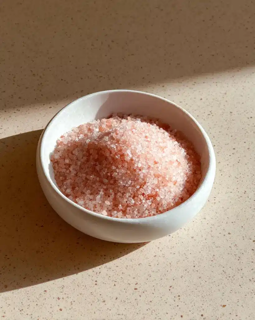 Bowl of coarse pink Himalayan salt used in the pink salt trick recipe on a stone countertop