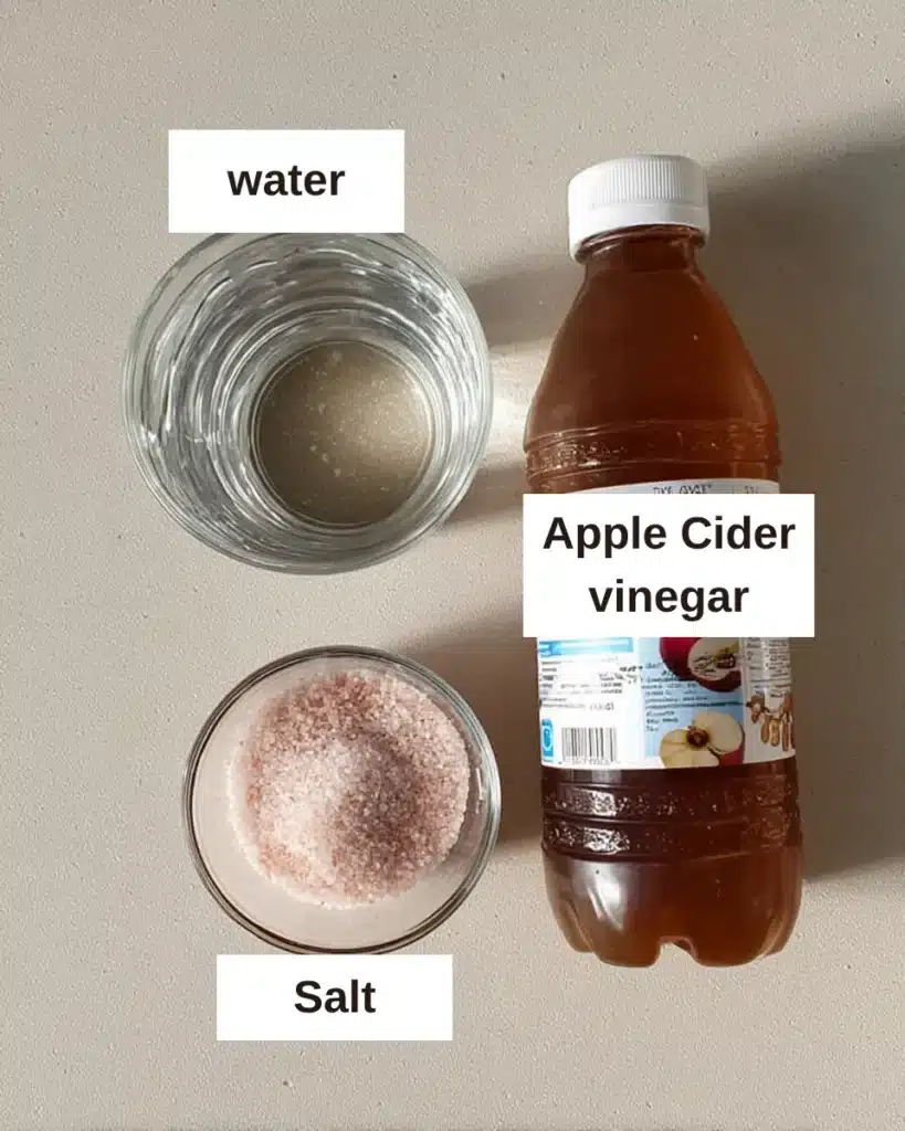 Flat lay of pink salt trick recipe ingredients: apple cider vinegar bottle, pink Himalayan salt, and a glass of water on a countertop