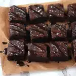 Date Brownies Recipe – Fudgy, Healthy, and Naturally Sweetened 7 Fudgy chocolate squares from a date brownies recipe, drizzled with glossy glaze and sprinkled with sea salt on parchment paper.