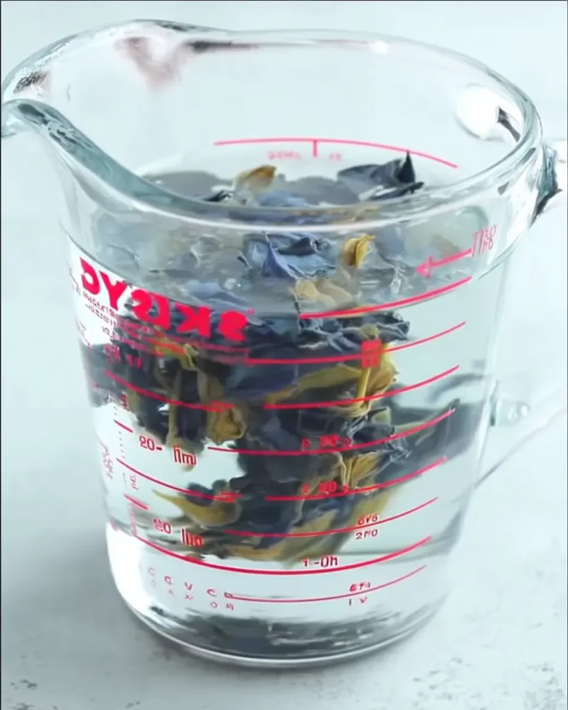 Butterfly Pea Tea Lemonade – Brilliant & Refreshing Recipe 15 Butterfly pea tea lemonade flowers steeping in water inside a glass measuring cup