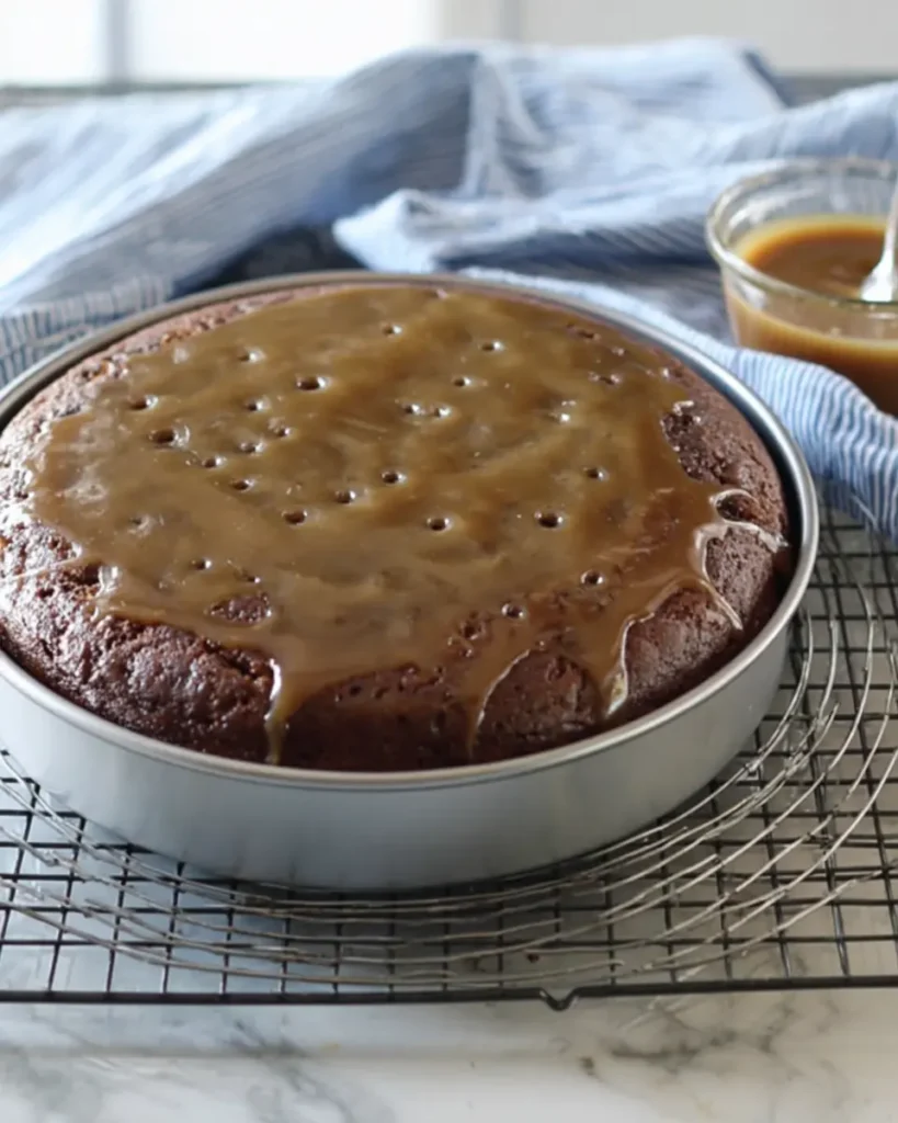 Sticky Date Cake Recipe – Moist, Rich & Perfect with Toffee Sauce 7 Sticky date cake in a round metal pan with toffee sauce poured on top and visible fork holes, resting on a cooling rack.