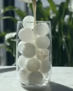Pouring milk over round ice spheres to begin the whipped honey coffee recipe in a tall clear glass