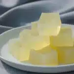 Pale yellow gelatin cubes on a white plate with glossy texture for a weight loss gelatin recipe.