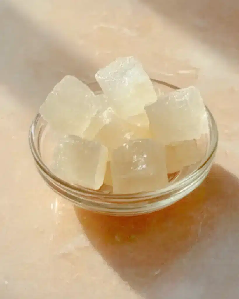 Gelatin Trick Ingredients for Satisfying, Light, Protein-Rich Snacking 1 Pale translucent gelatin cubes in a glass dish on a soft beige surface