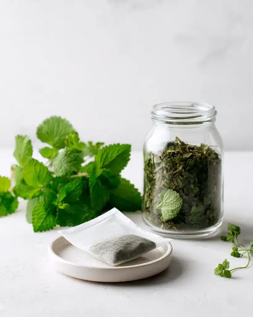 Fresh lemon balm sprigs with dried leaves in a jar and an unbranded tea bag on white