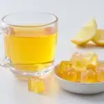 Warm gelatin drink beside translucent gelatin cubes and lemon wedges on a white background