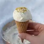 Hand holding viral snow ice cream in a waffle cone with nut topping, made using the salted snow bowl method.