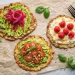 Cottage Cheese Breakfast Rounds topped with avocado, tomatoes, pickled onions, and raspberries on parchment
