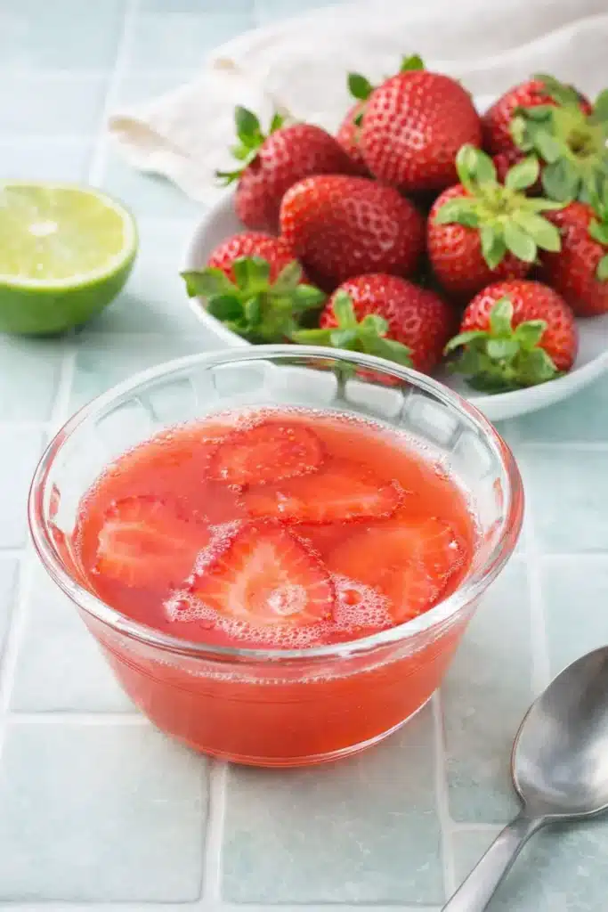 Strawberry Gelatin with Fresh Strawberries, Lime, and Honey 17 Strawberry Gelatin in a glass bowl with sliced strawberries, fresh berries, and lime nearby