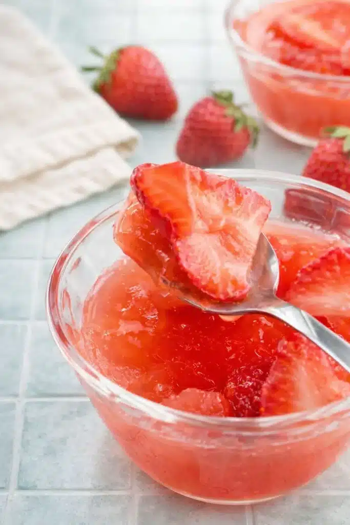 Strawberry Gelatin with Fresh Strawberries, Lime, and Honey 20 Spoon lifting a bite of Strawberry Gelatin with real strawberry slices from a glass bowl